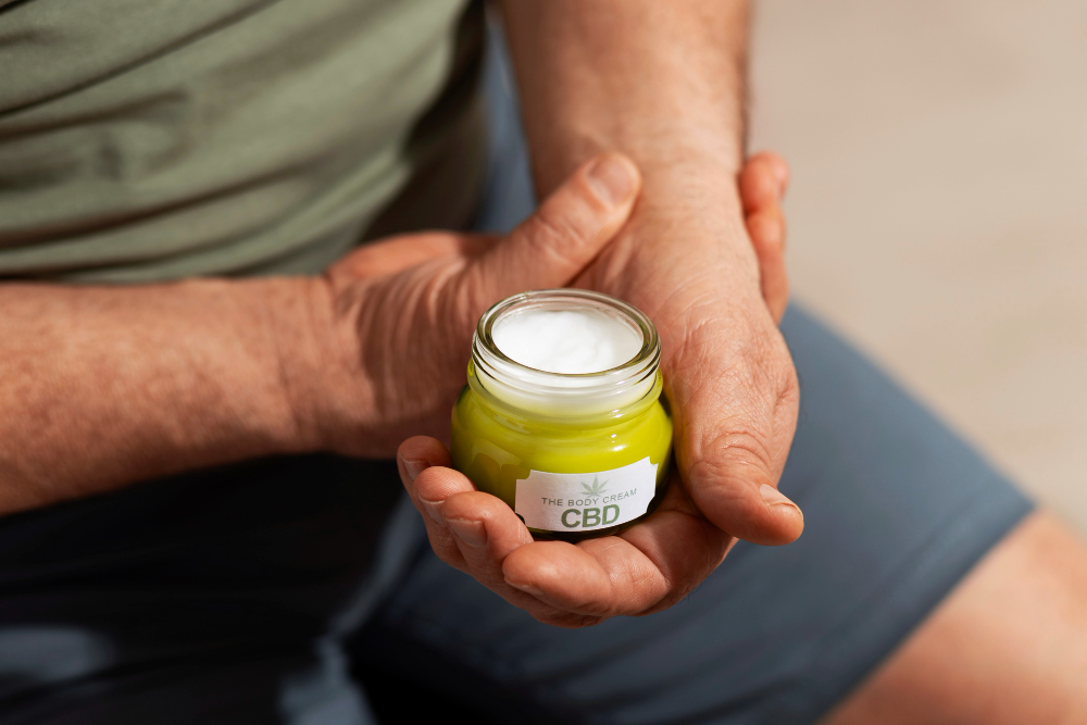 A man holds a jar of green CBD muscle gel labeled "Recover Faster with CBD Muscle Gel by Zentric Life.