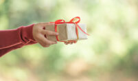 A person displays a small gift box with a red ribbon, illustrating the healing meaning behind everyday gifts.